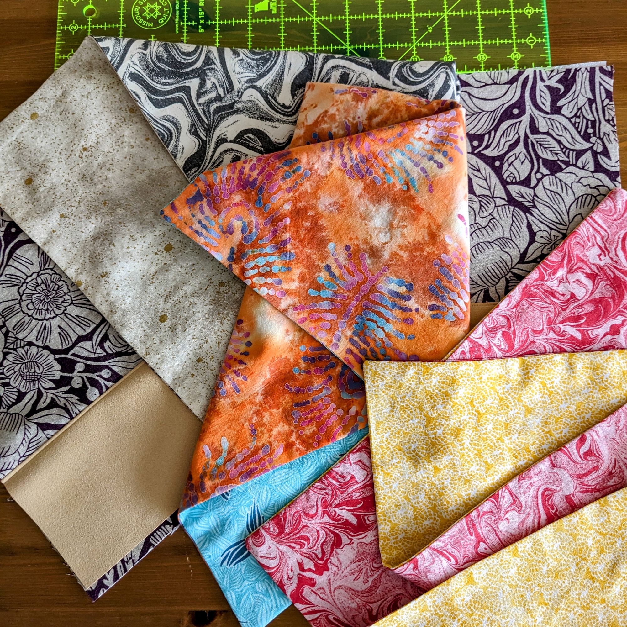 Colourful cotton dinner napkins on a wooden background with a quilting rule above.
